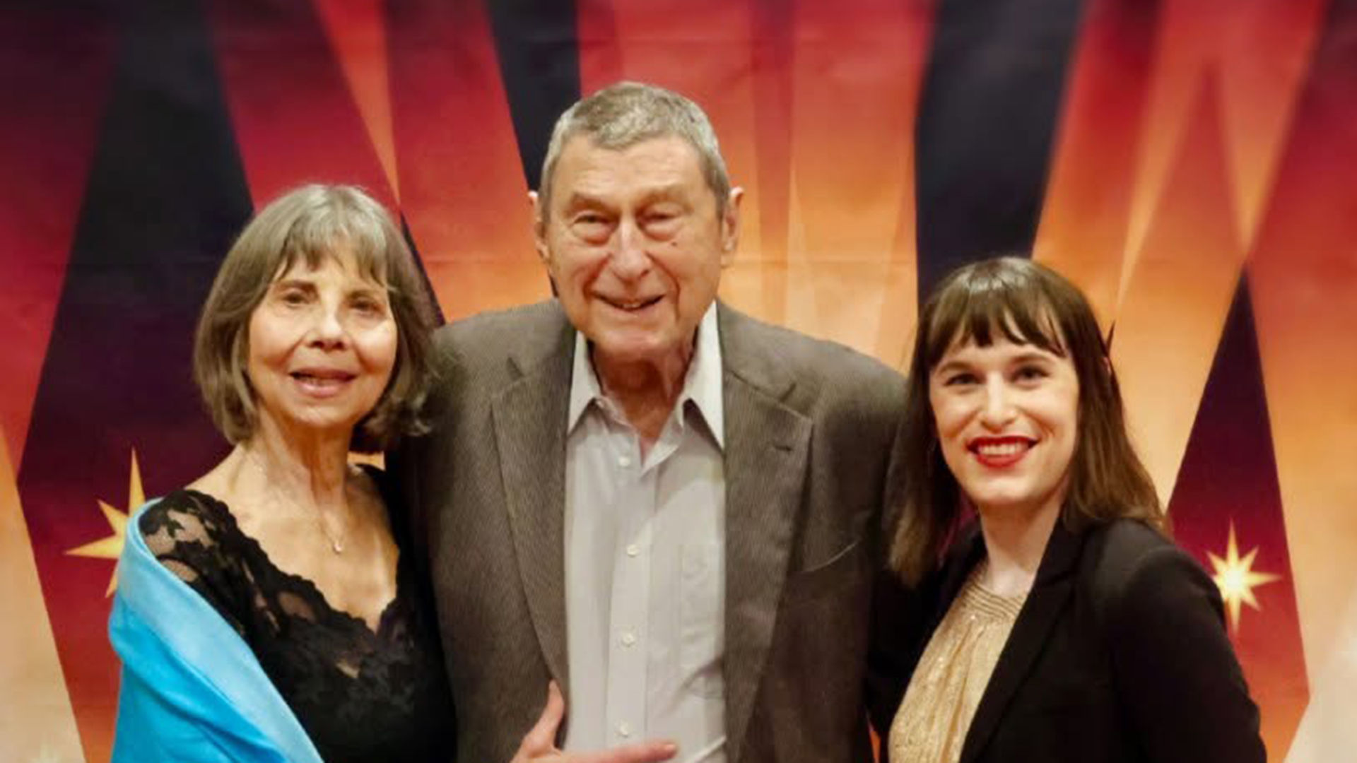 Three people smiling and posing together in front of a colorful star-patterned backdrop.