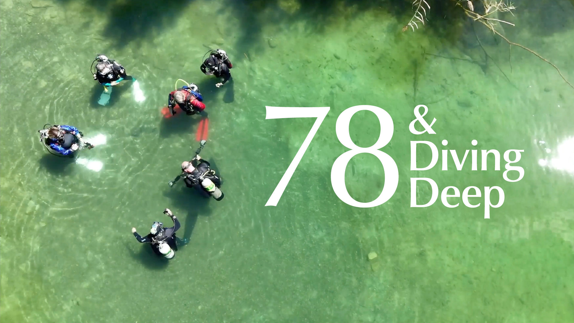 Aerial view of six scuba divers in clear water with the text "78 & Diving Deep" on the right side.