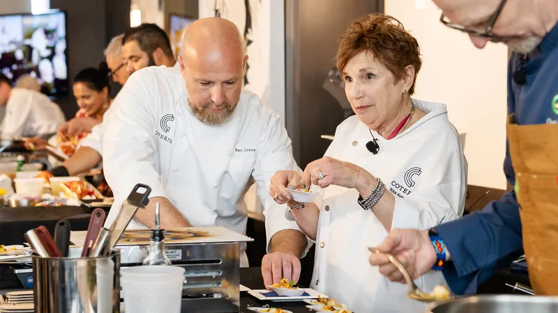 Chefs in a kitchen prepare dishes with focus and collaboration, surrounded by cooking tools and ingredients.