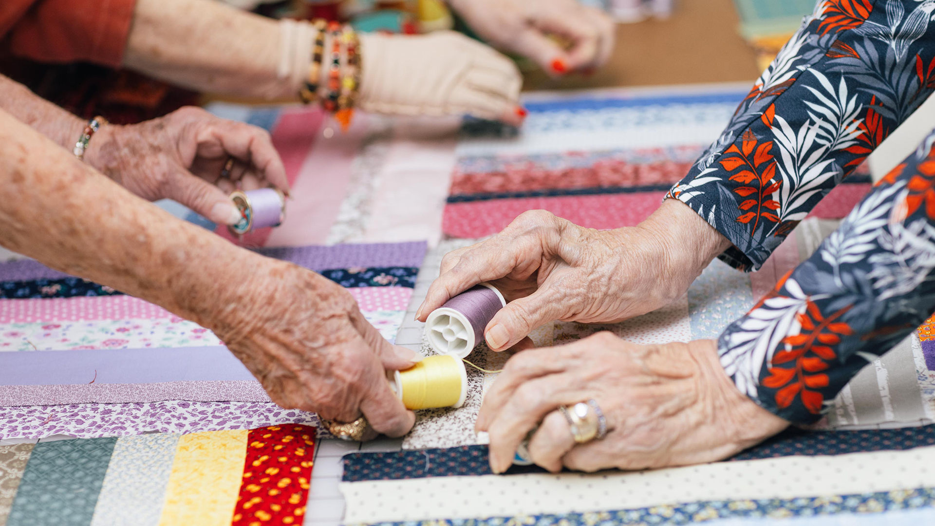 The hands of three Holiday residents work on crafting with colorful fabric and thread.