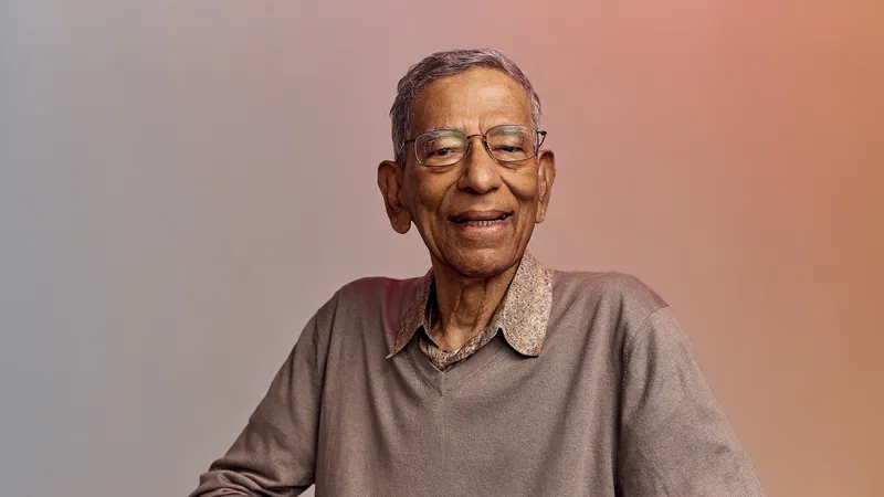 Older adult man with glasses and a warm smile, wearing a light gray sweater over a collared shirt, against a softly colored gradient background.