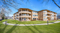 Three-story apartment building with wooden exterior, balconies, and a surrounding green lawn under a clear blue sky., click to stop animation