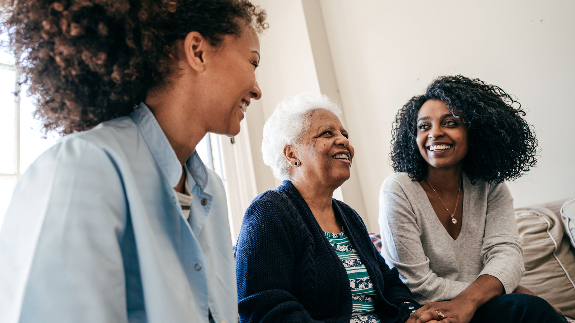 "Older woman with her two daughters smiling and laughing together