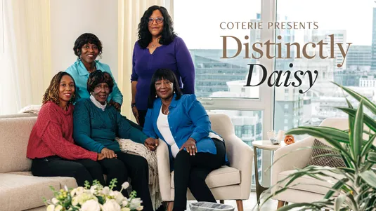Five women smiling in a cozy room with city view; text reads "Coterie Presents Distinctly Daisy."
