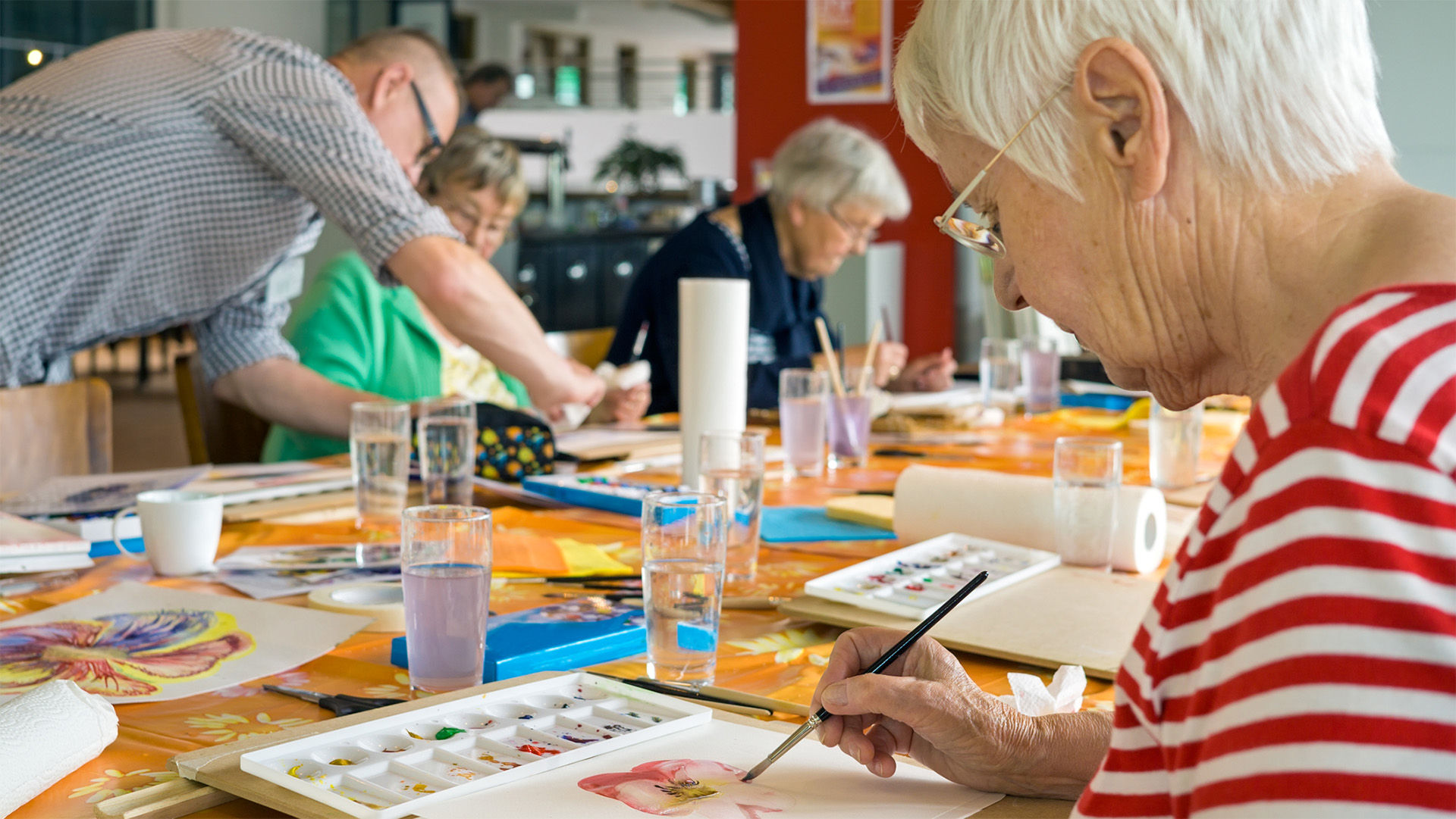 Three senior residents painting with watercolor in an art class with the help of an instructor.