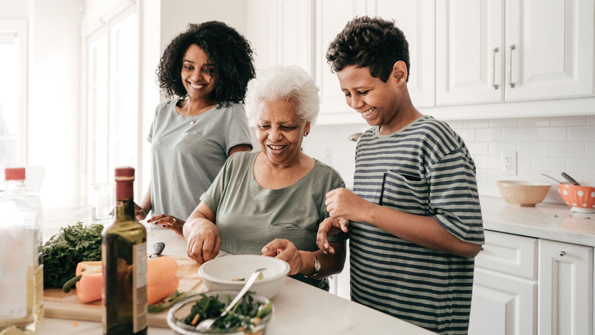 Senior cooking in her kitchen with her adult daughter and teenage grandson.