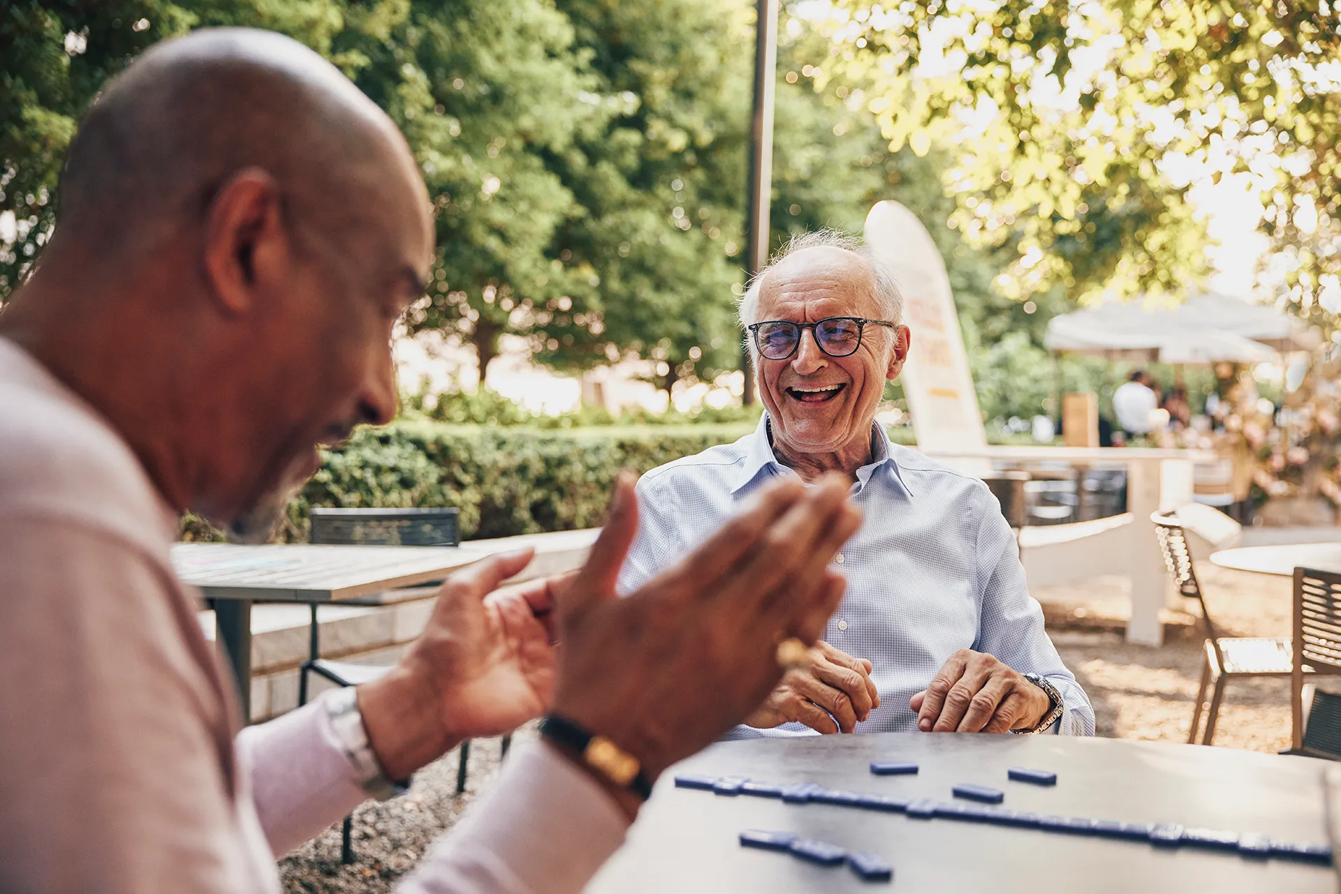 Two men in a park playing domnios, talking and laughing