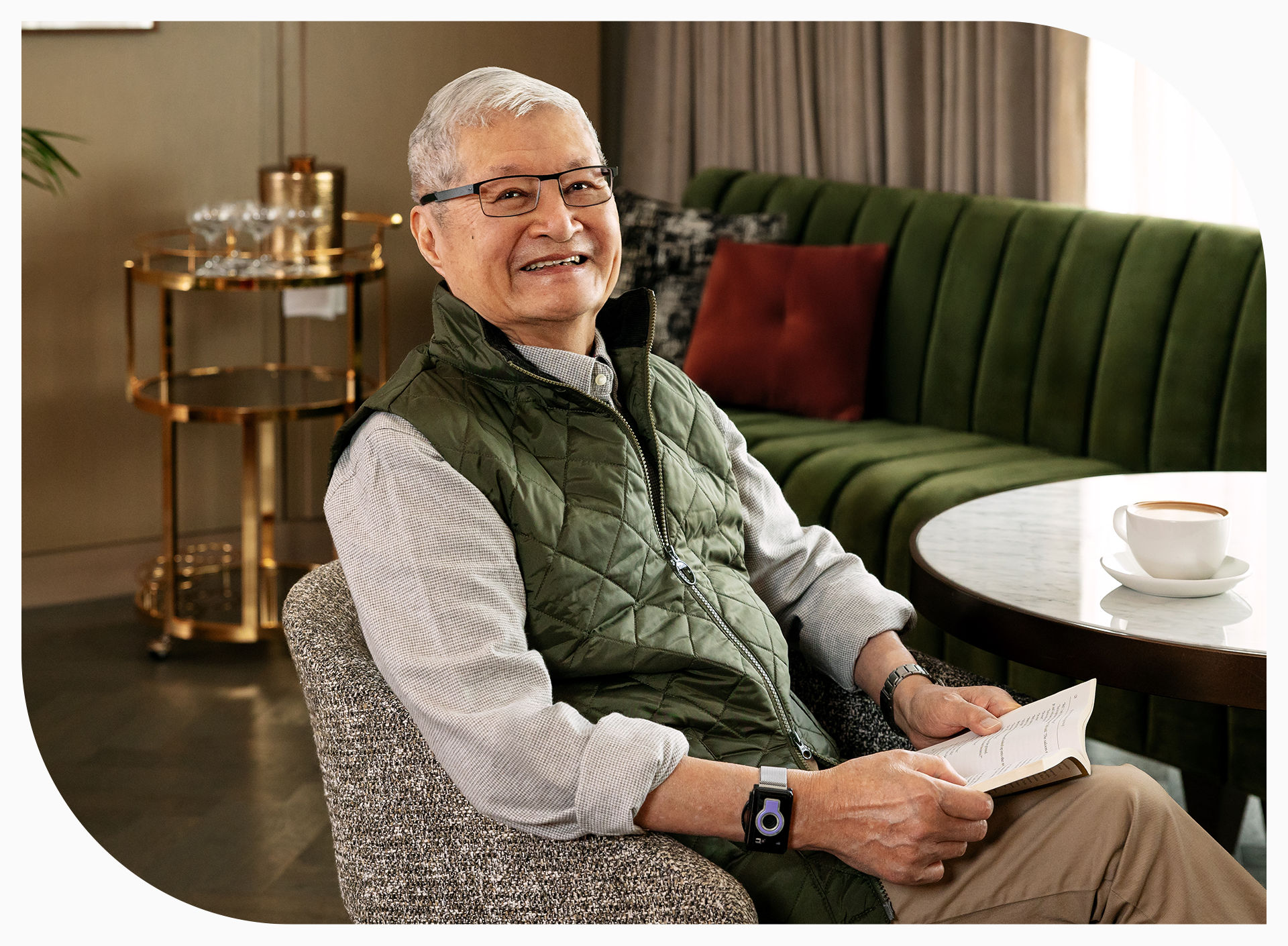 Coterie resident Williams Lee sitting in lounge smiling while drinking coffee and reading.