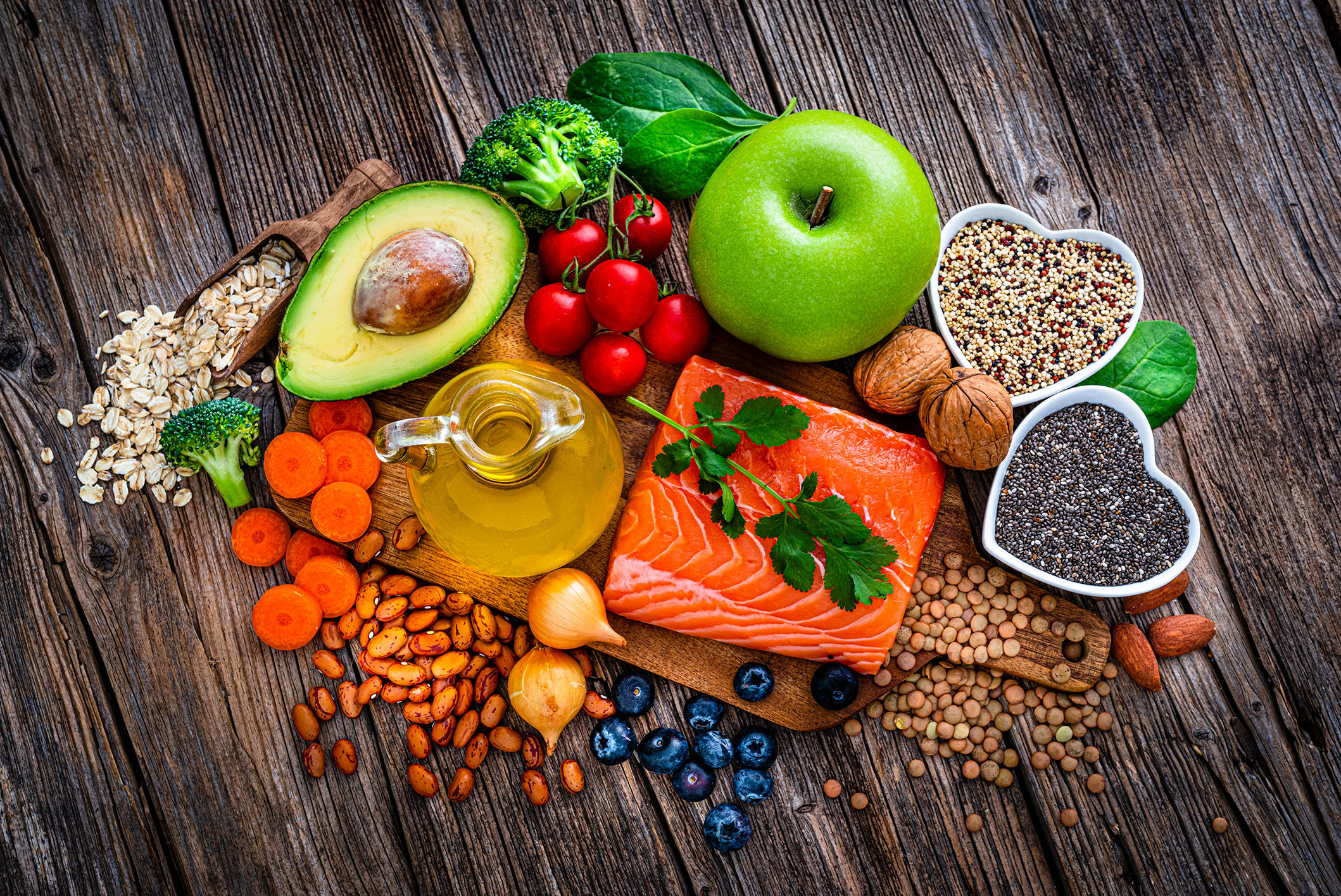arrangement of healthy who foods lie apples, avocados, salmon, broccoli, carrots, chia seeds and oats