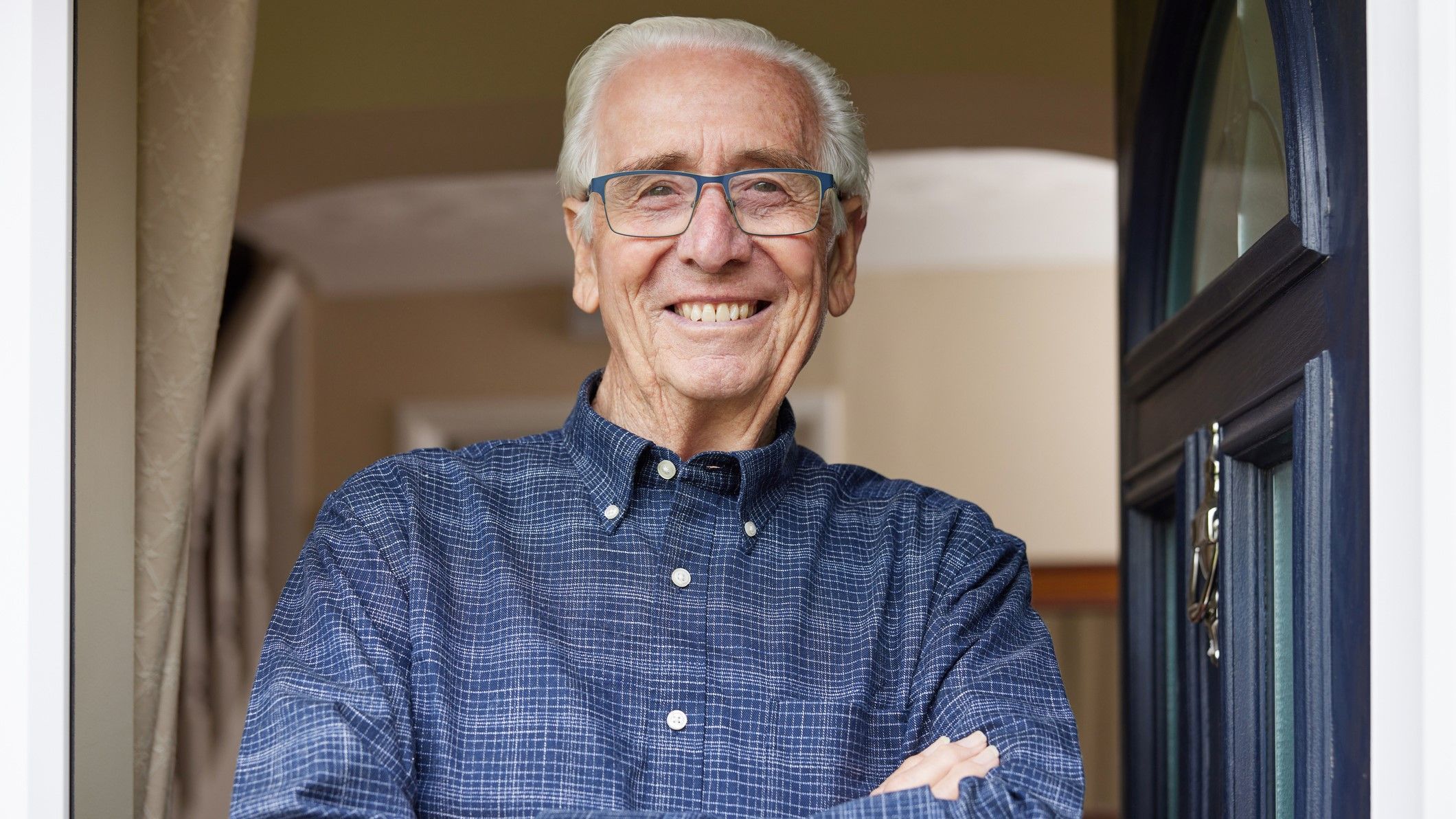 Smiling senior man standing at open front door of house