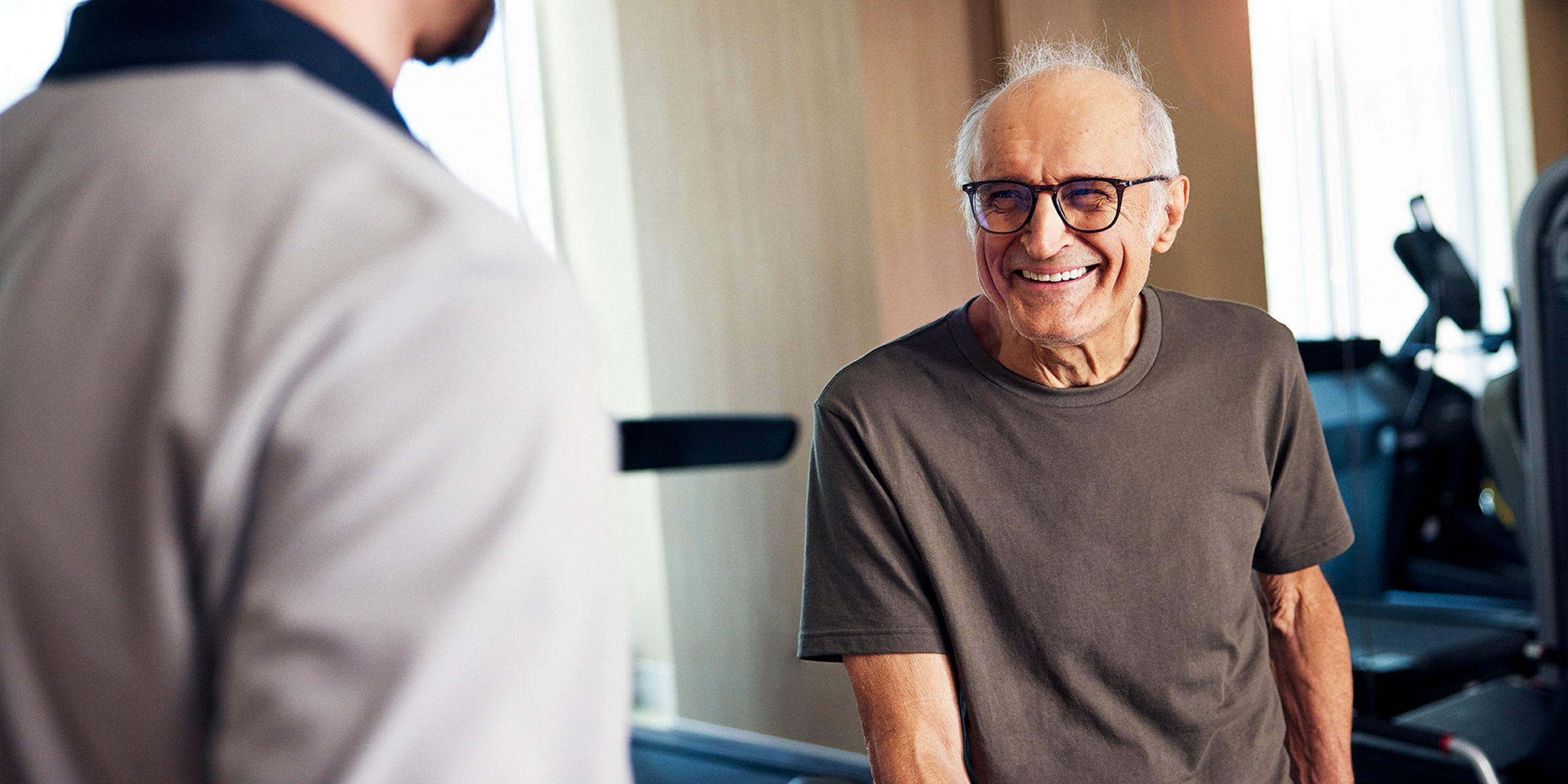 Older adult smiling at rehab coach with fitness equipment behind him