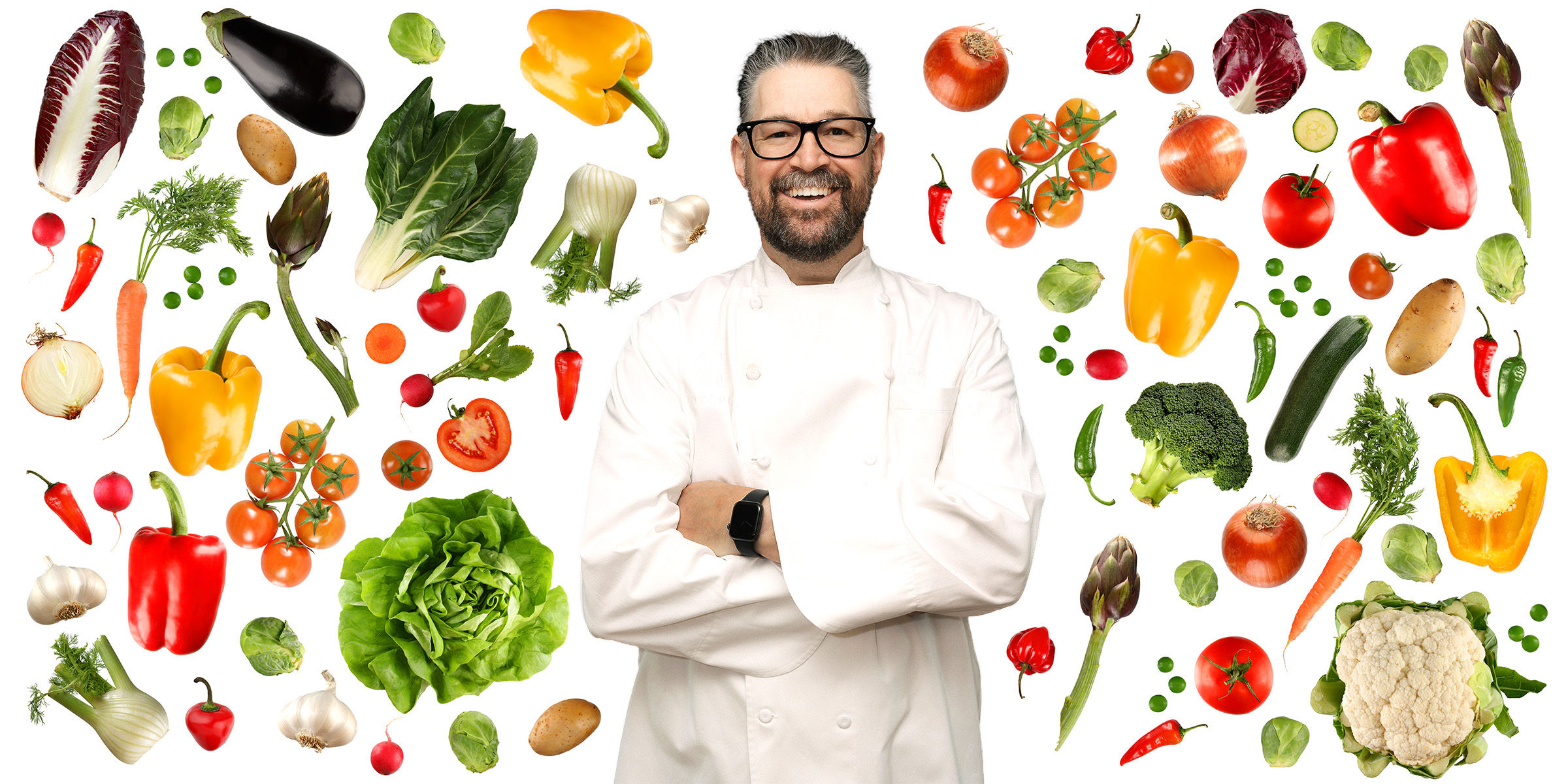 Chef Chad Welch smiling with arms crossed surrounded by vegetables