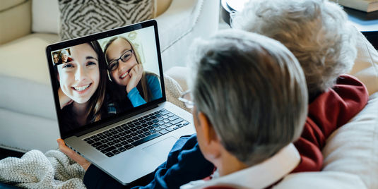 Older couple video chatting with their granddaughters via a computer on their lap