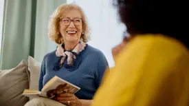Group of people with a mixed age range talking and laughing while having a book club meeting.