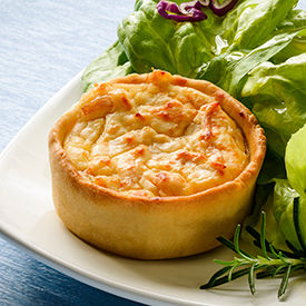 A small quiche with a side salad on a ceramic white plate on a blue tablecloth