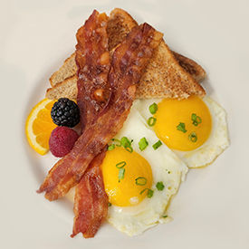 Eggs, bacon and fruit on a white plate