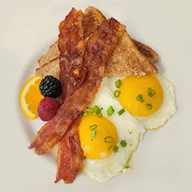 Eggs, bacon and fruit on a white plate