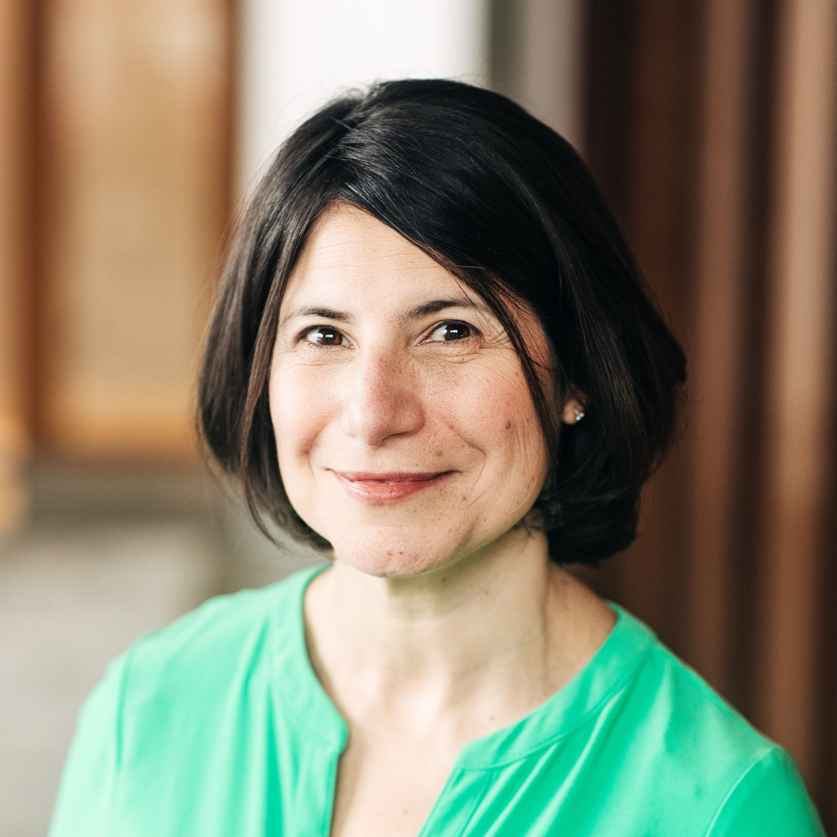 A woman with short dark hair in a green blouse smiles gently at the camera, with a softly blurred background.