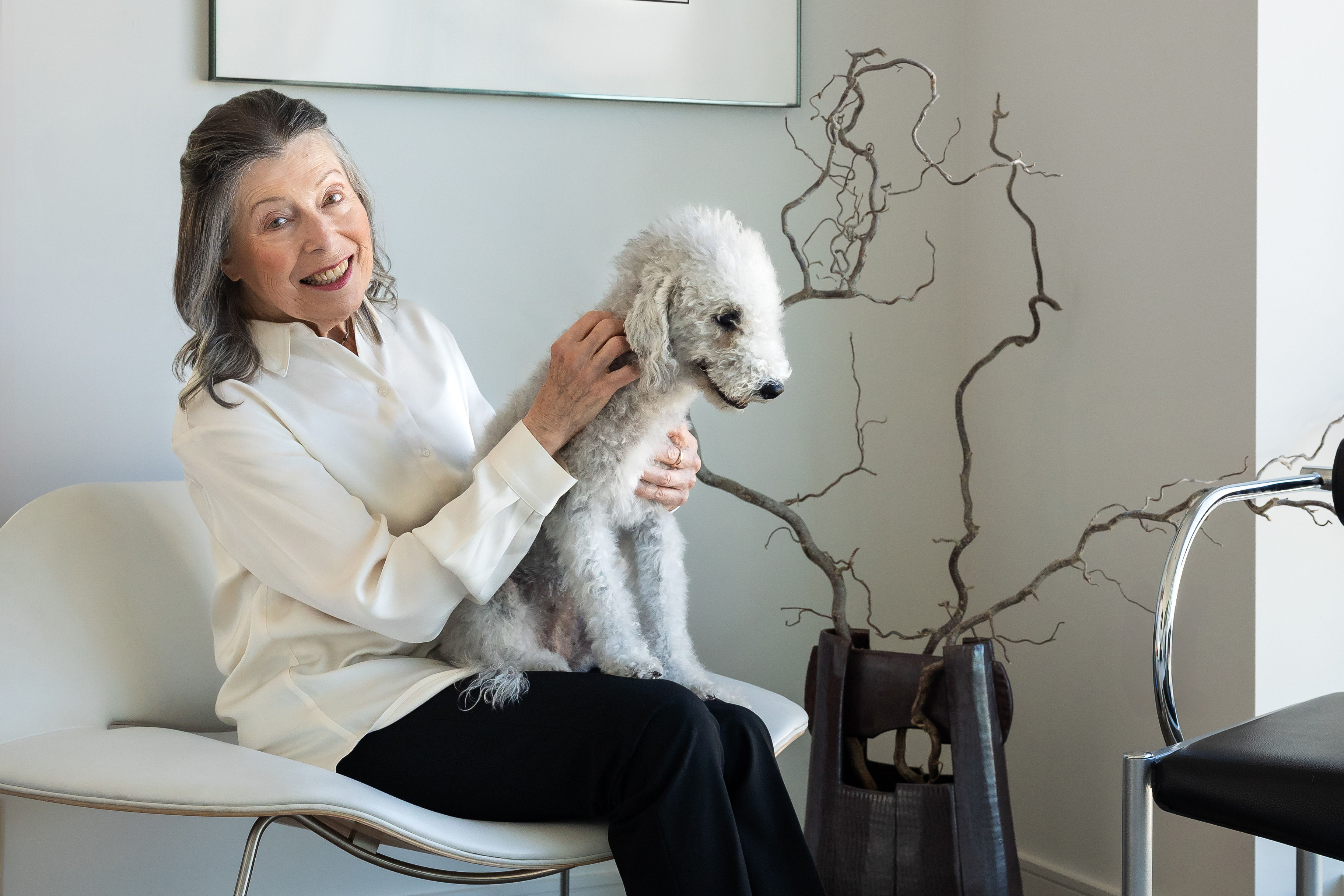 Senior woman laughing while sitting in chair holding a fluffy white dog