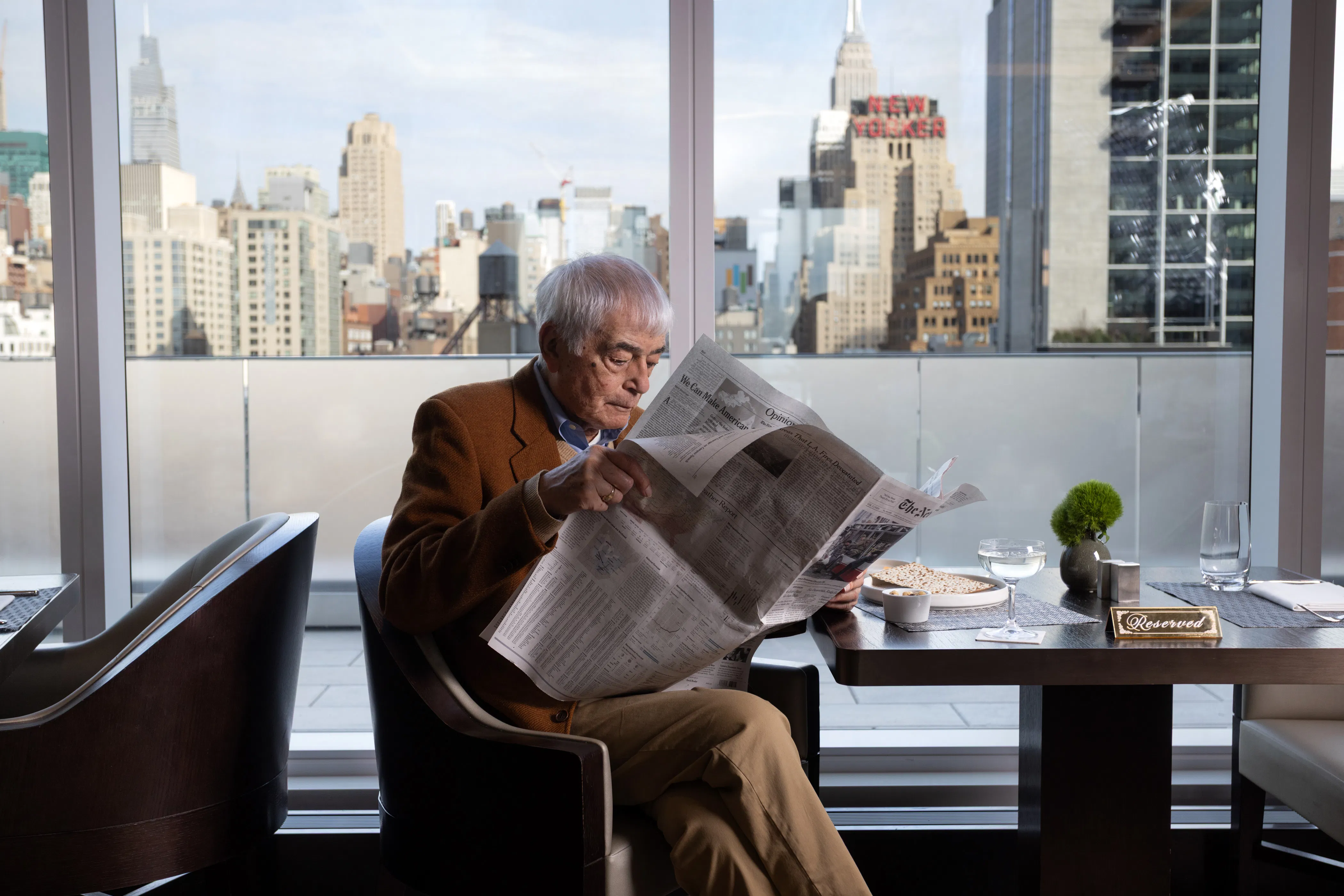 senior man sitting, reading the newspaper with the New York City skyline view behind him