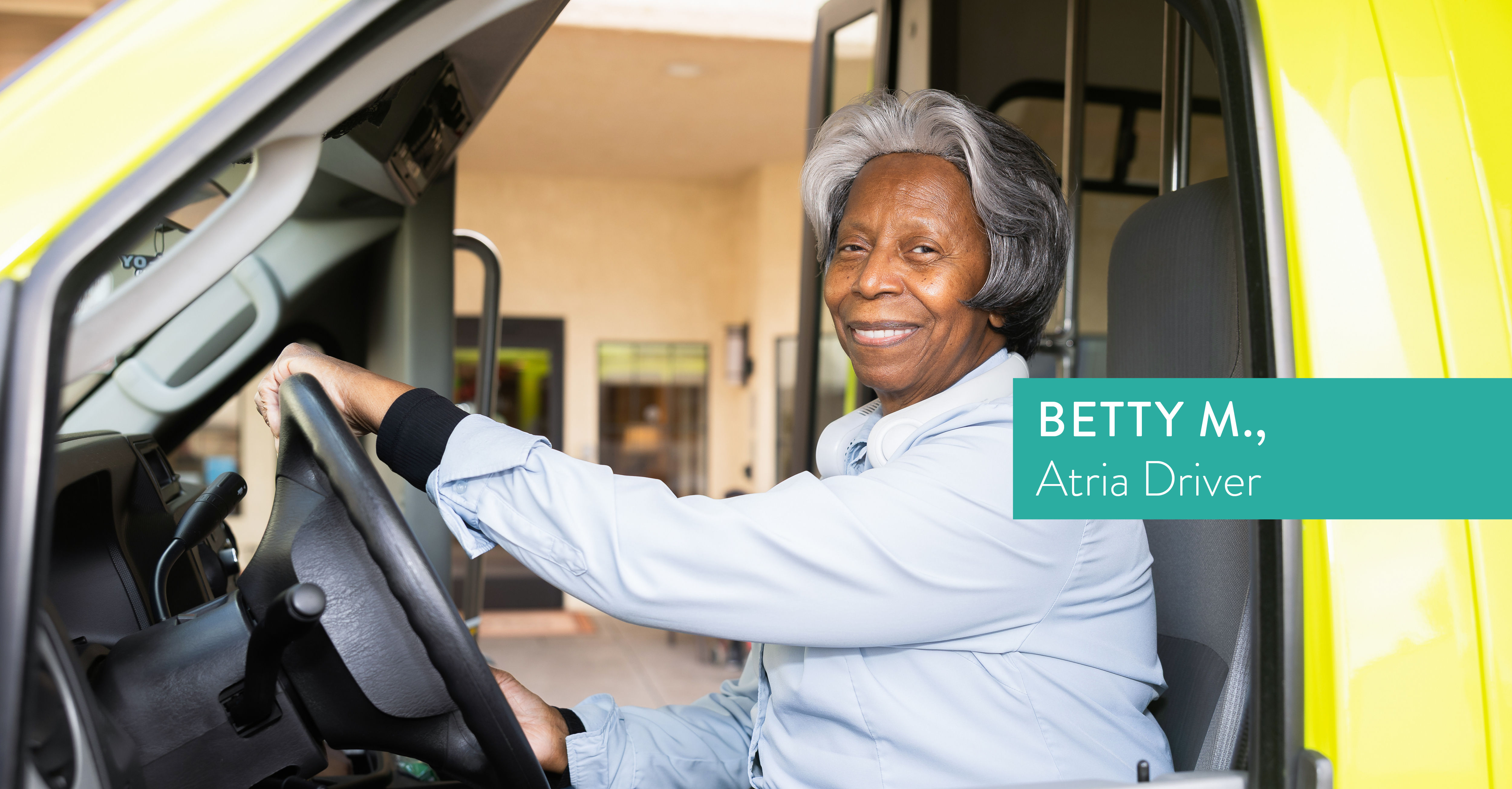 Older woman smiling while seated in the driver's seat of a yellow vehicle, wearing a light blue shirt. Text reads: "BETTY M., Atria Driver."