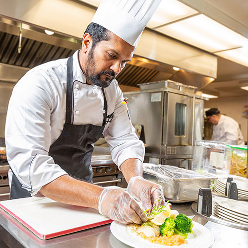 chef dressed in his regalia preparing a meal in a fully equipped industrial kitchen