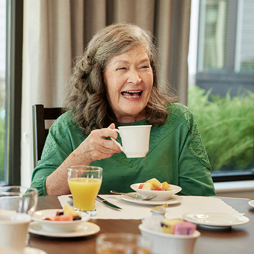 senior woman laughing while enjoying breakfast and coffee in a dining room