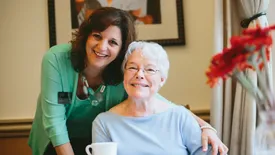 Atria employee smiling alongside resident who's drinking coffee