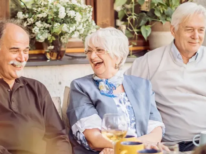 Three senior friends enjoy dinner together over smiles.