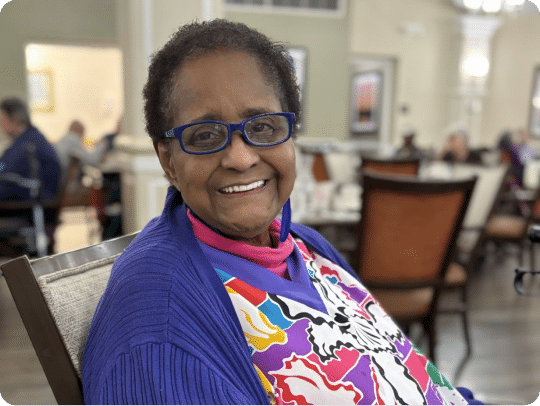 Senior resident sitting in dining room looking at camera smiling.