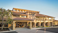 A two-story building with a mix of stone and stucco facade, featuring a red-tiled roof and balconies, set against a clear blue sky., click to stop animation