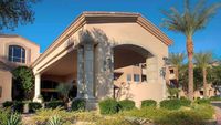 Elegant building entrance with large columns, archway, and manicured landscaping, set against a clear blue sky., click to stop animation