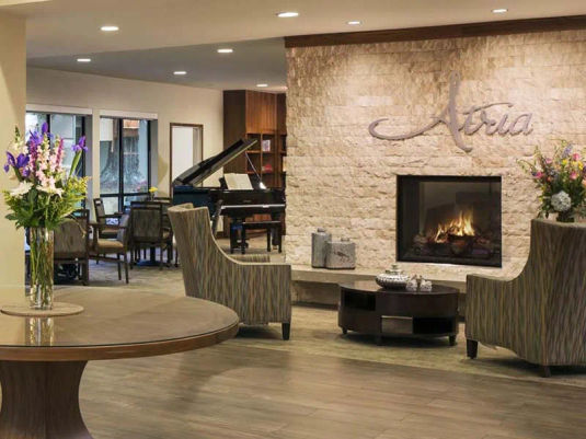 Atria El Camino Gardens lobby, with large stone wall fireplace and grand piano.