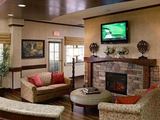 Atria Grapevine Senior Living living room with a fireplace, seating and a tv over the fireplace.