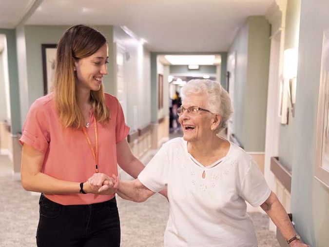Physical therapist helping resident walk down hallway.