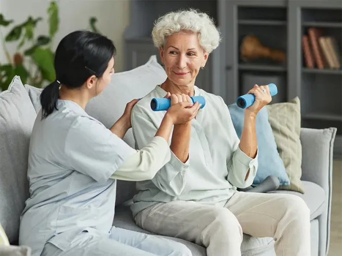 Senior resident using hand weights and being helped by a physical therapy aide.