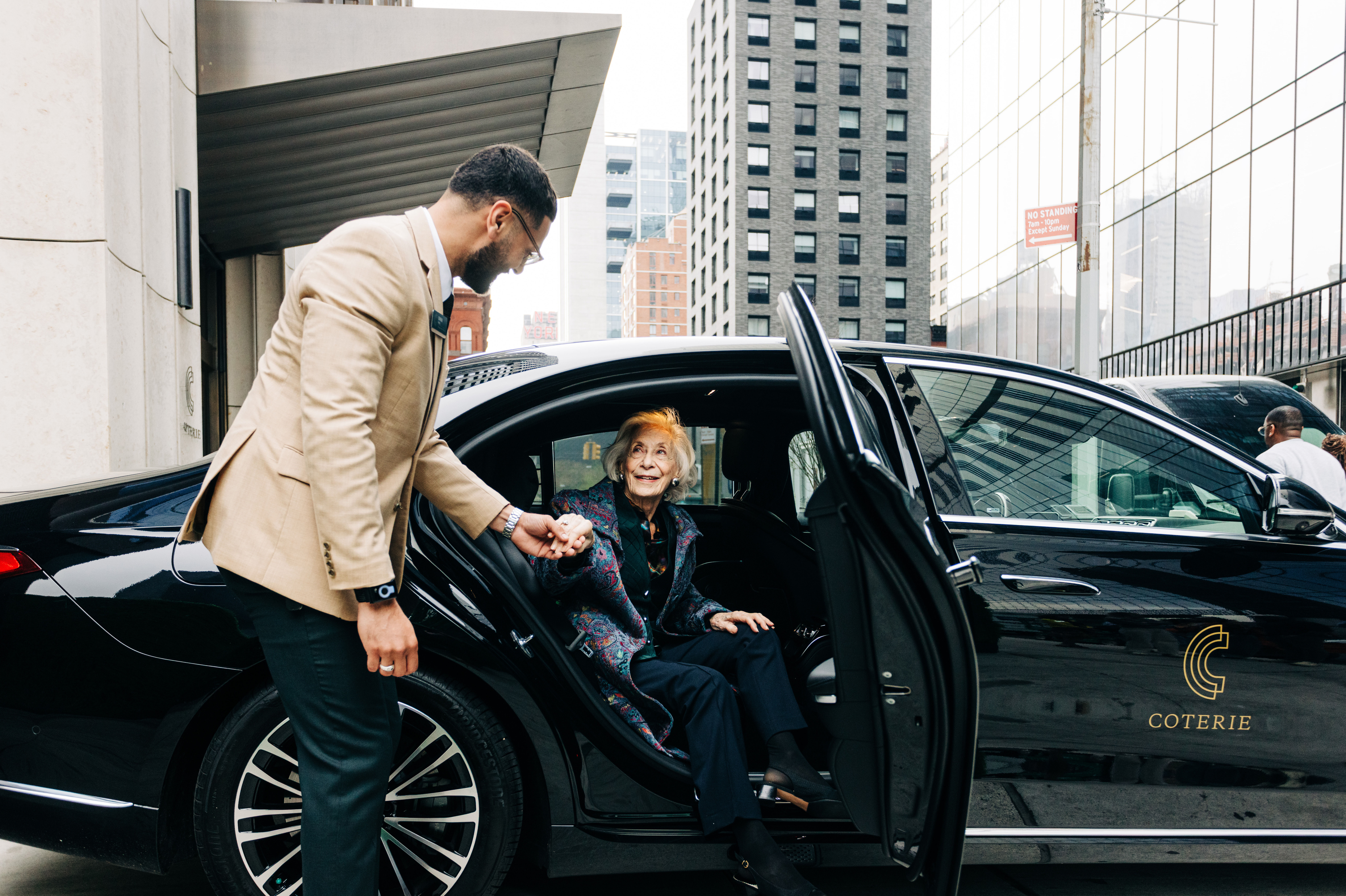 chauffeur in beige suit assisting senior out of a courtesy vehicle in a New York senior living community
