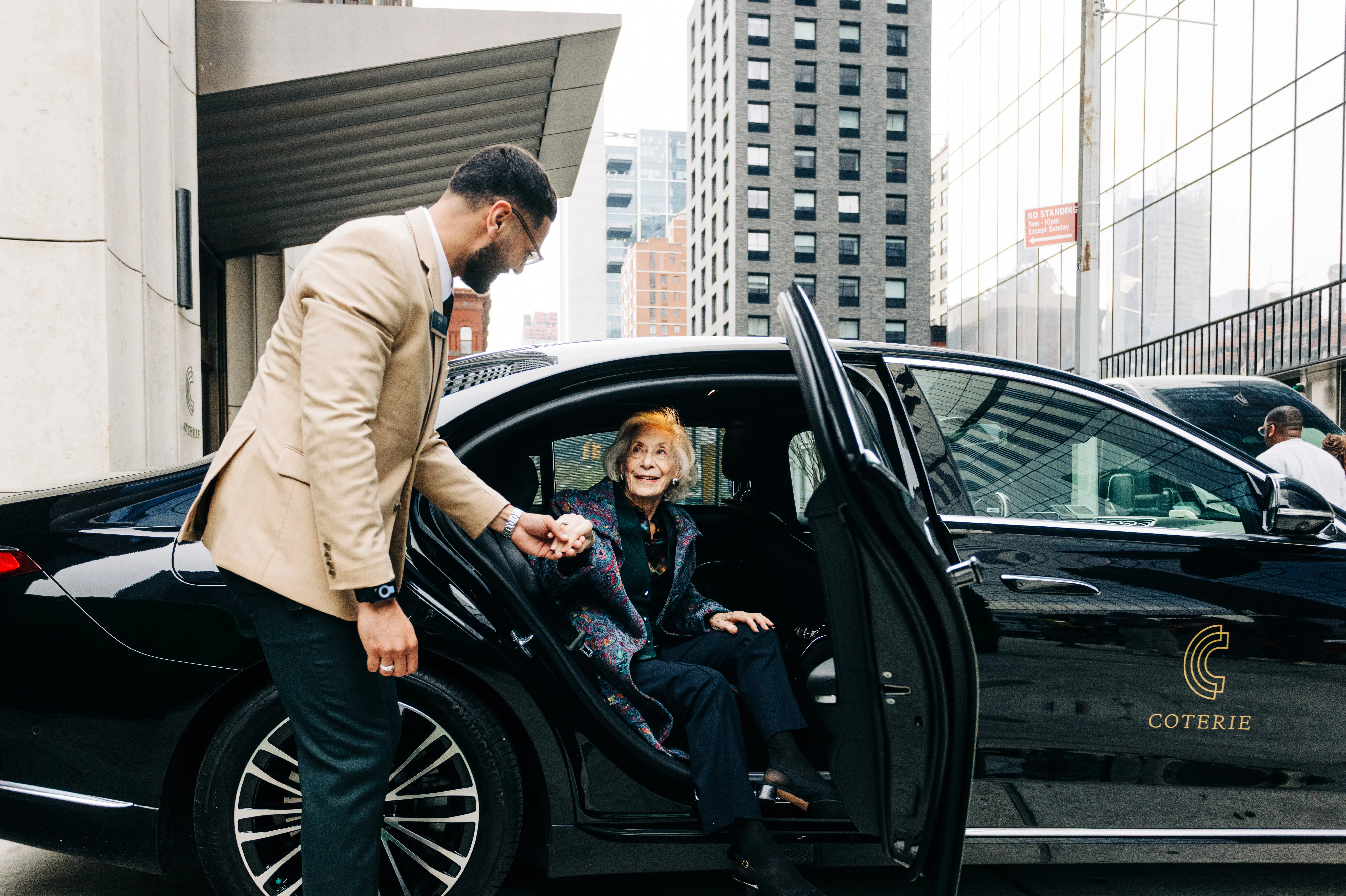 chauffeur in beige suit assisting senior out of a courtesy vehicle in a New York senior living community
