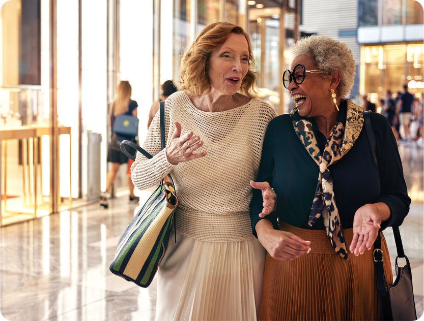 two women arms interlocked walking through the building together laughing and smiling