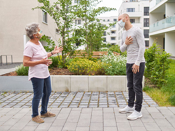 Image of an older woman and young man wearing masking and talking