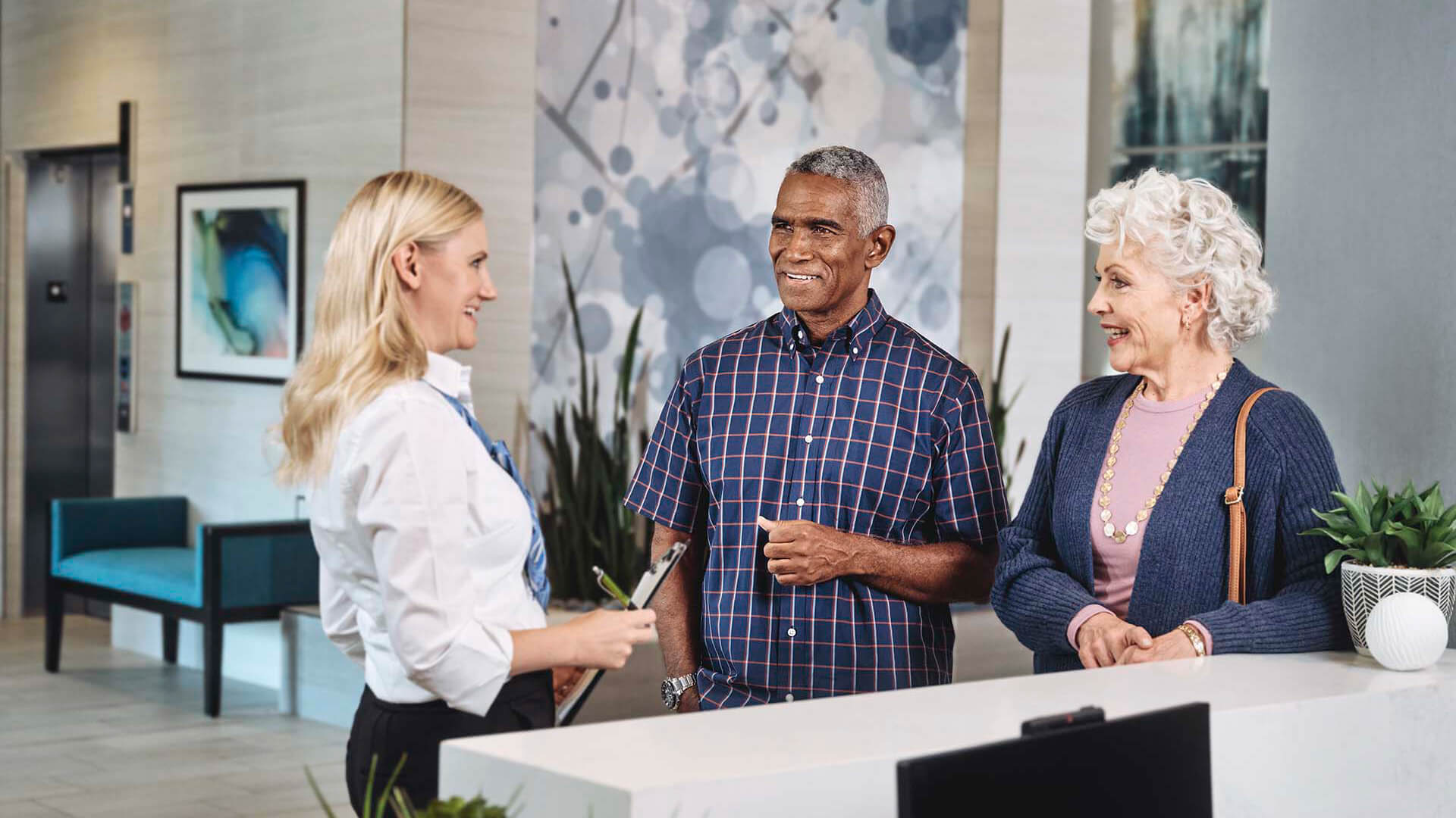 Photo of an Atria Senior Living Employee greeting two older people at the front desk