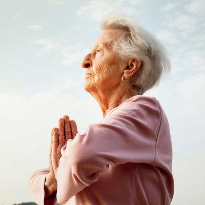 senior woman, 88 years old, active and flexible, practising yoga at a lake at a sunny summer morning, folding hands