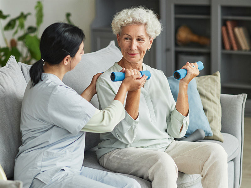 Therapist assisting an older woman to use weights