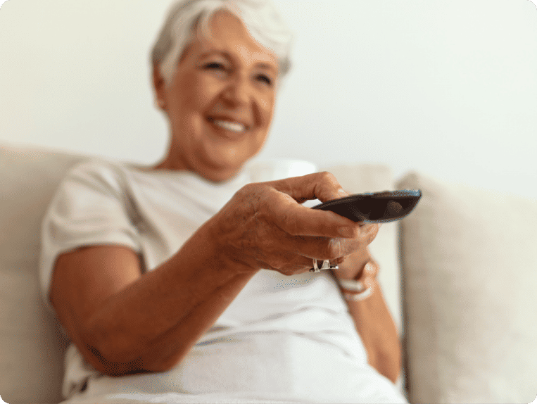 Blurred older woman sitting on couch points an in-focus remote just off screen