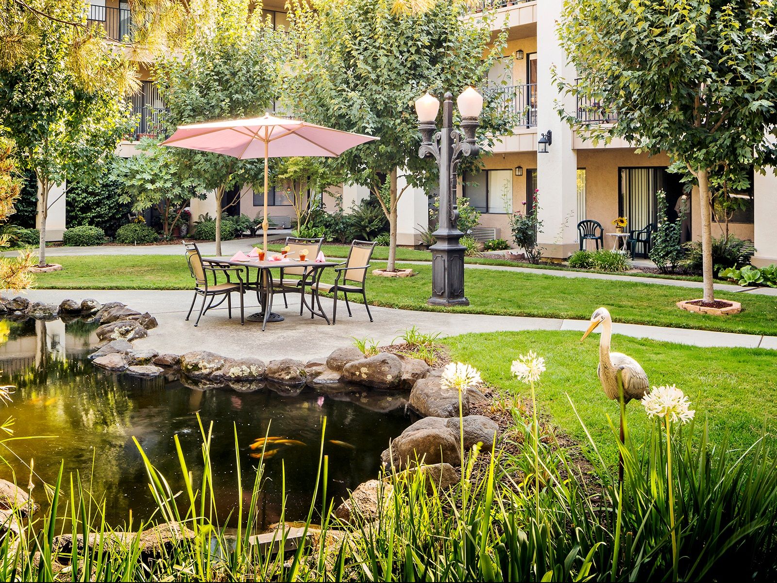 Courtyard outside Atria Carmichael Oaks, featuring a beautiful water feature with koi bond and walking paths surrounded by lush greenery and a stork statue