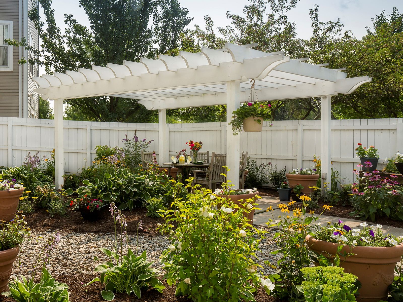 Shaded slat overhang above a table set with orange juice and pastries, all surrounded by a lush assortment of flowers and plants