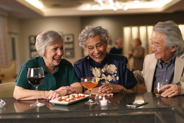 Three female senior living residents enjoying wine and appetizers in a lounge.