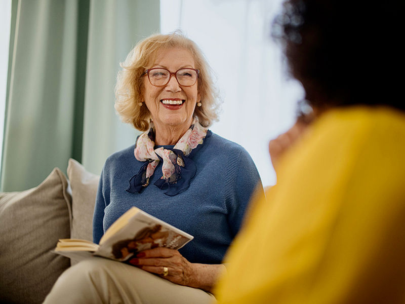 Group of people with a mixed age range talking and laughing while having a book club meeting.