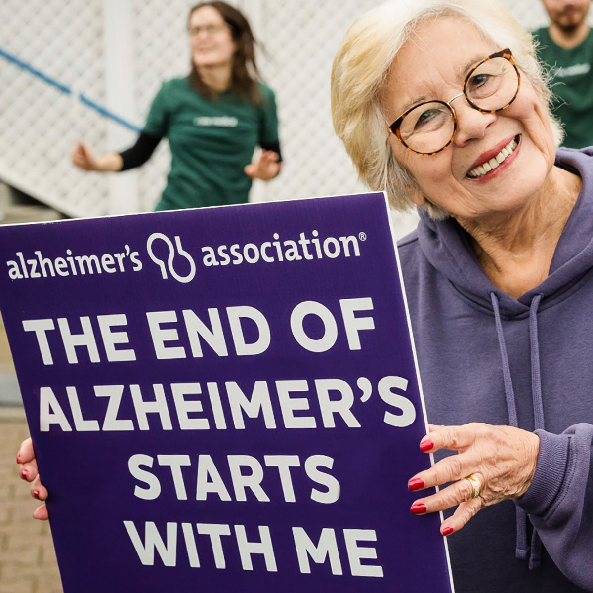 Older woman smiling at the camera and holding a sign that says The End of Alzheimer's Starts with Me