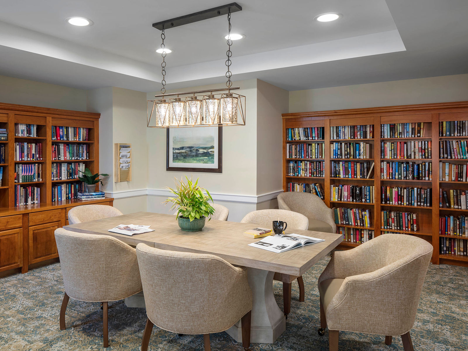 Library with shelves of books and a cream-colored table in the center surrounded by comfortable seating